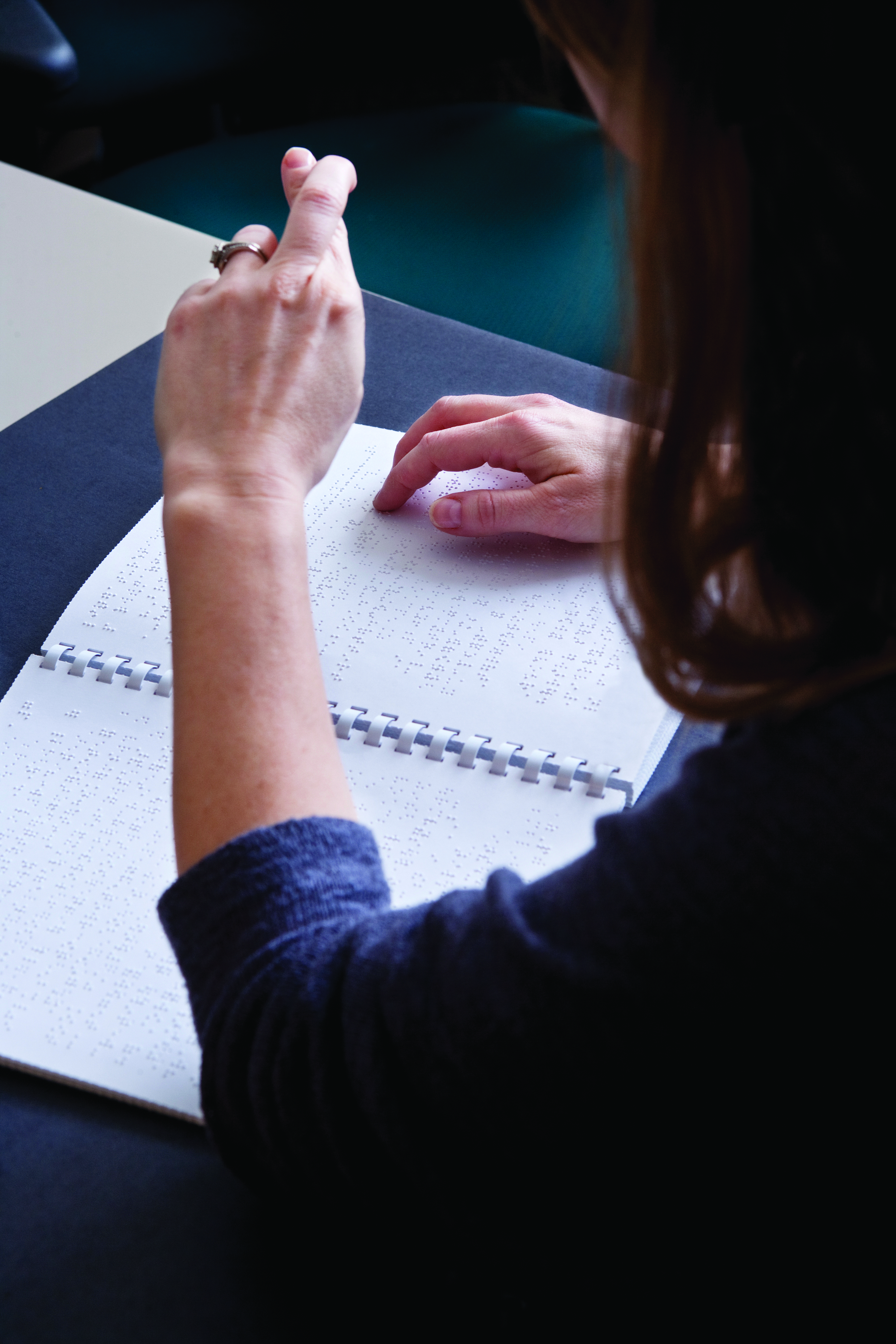 A person uses one hand to read braille, and the other to demonstrate sign language.