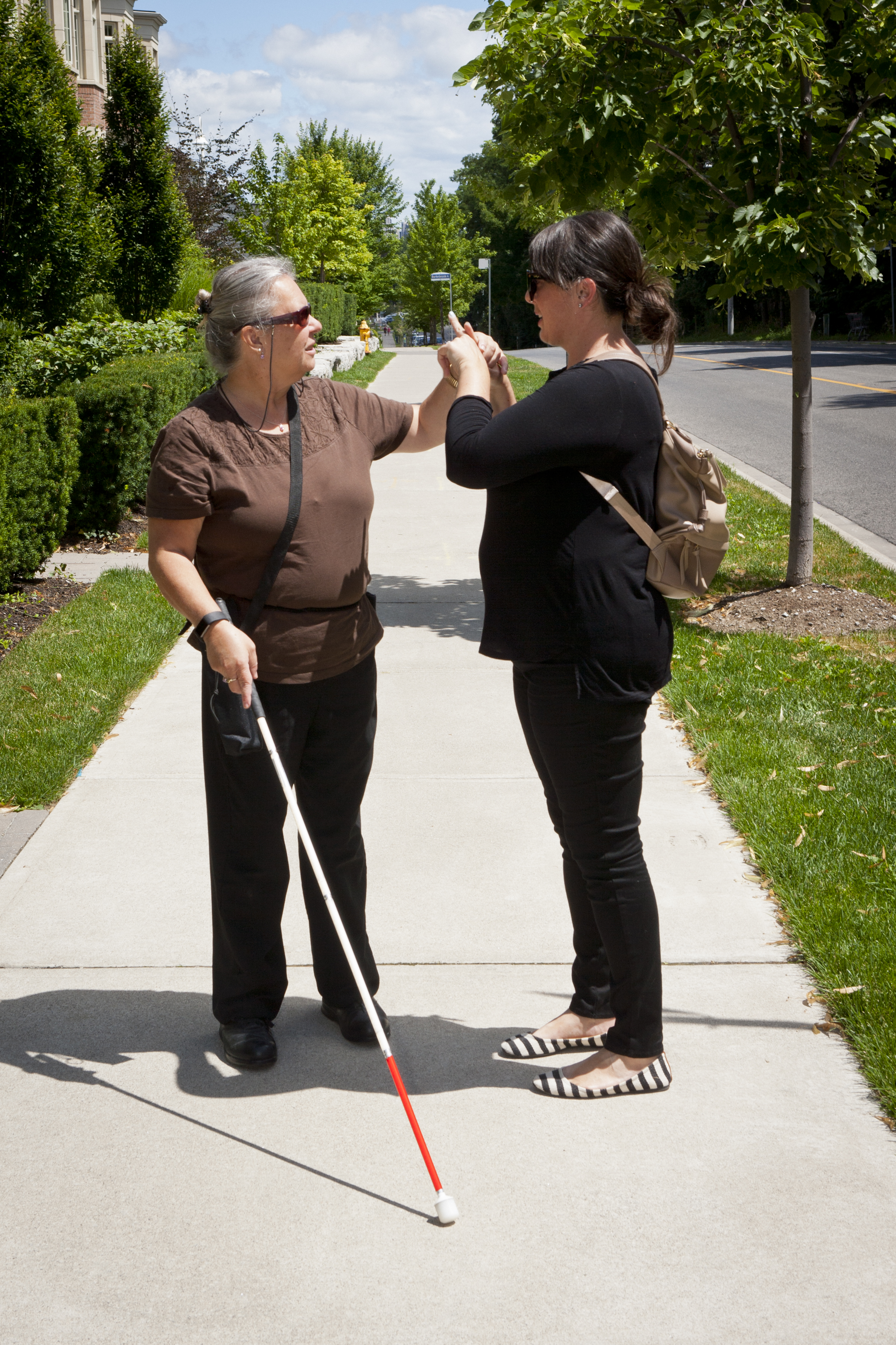 An intervenor and client stand outside and use tactile ASL to communicate.