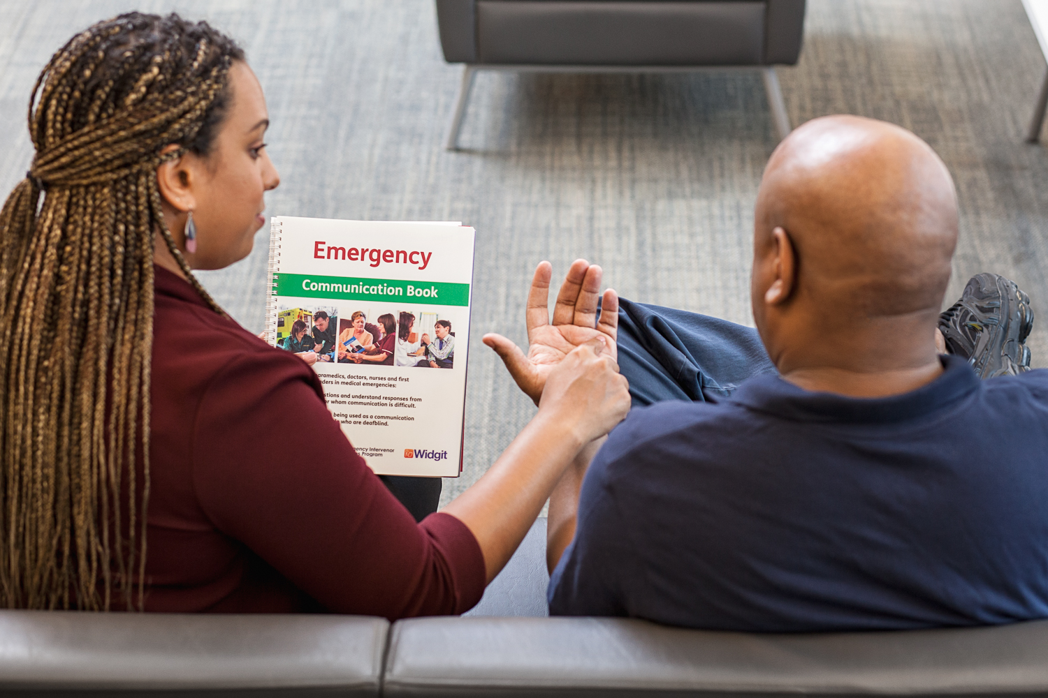 An intervenor uses print on palm to communicate with a client. In one hand she holds the DBCS Emergency Communication Book.