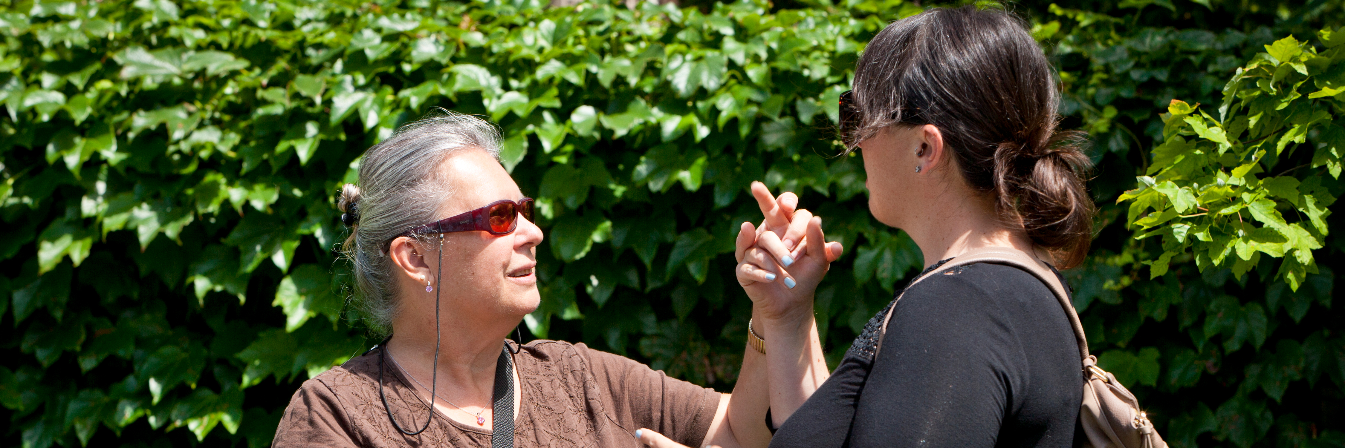 A DBCS staff member and client stand outside on a sunny day and use tactile ASL to communicate.