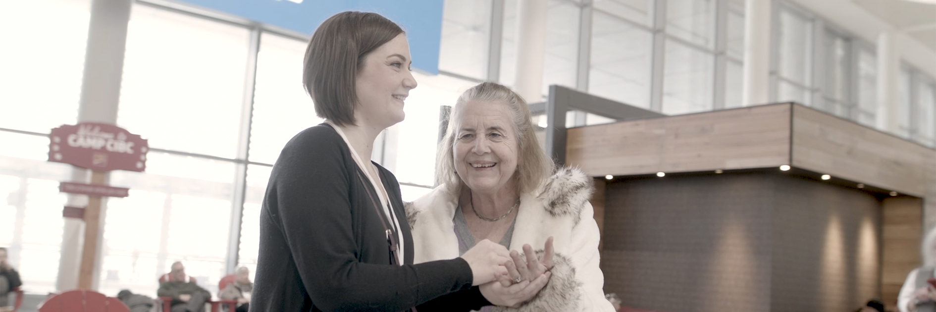 Penny, a person who is Deafblind, and her intervenor smile as they communicate using two-hand manual.