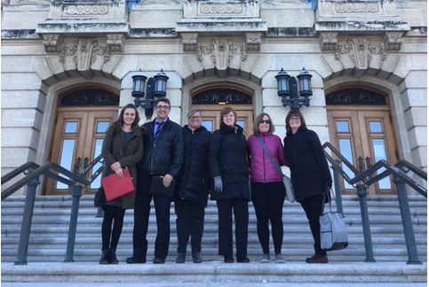 DBCS staff and government representatives from Saskatchewan stand outside a government building.