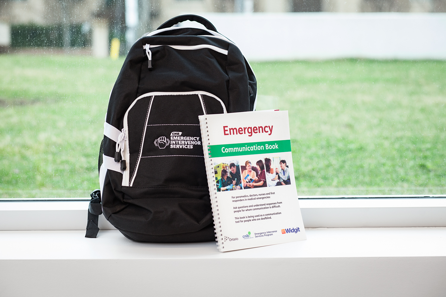 The DBCS Emergency Communication Kit. A black backpack with a book resting against it called, "Emergency Communication Book".