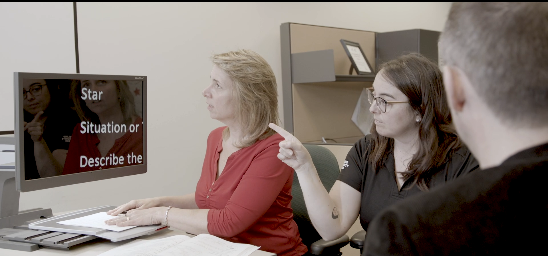 Two DBCS Staff members work with a client using a CCTV.