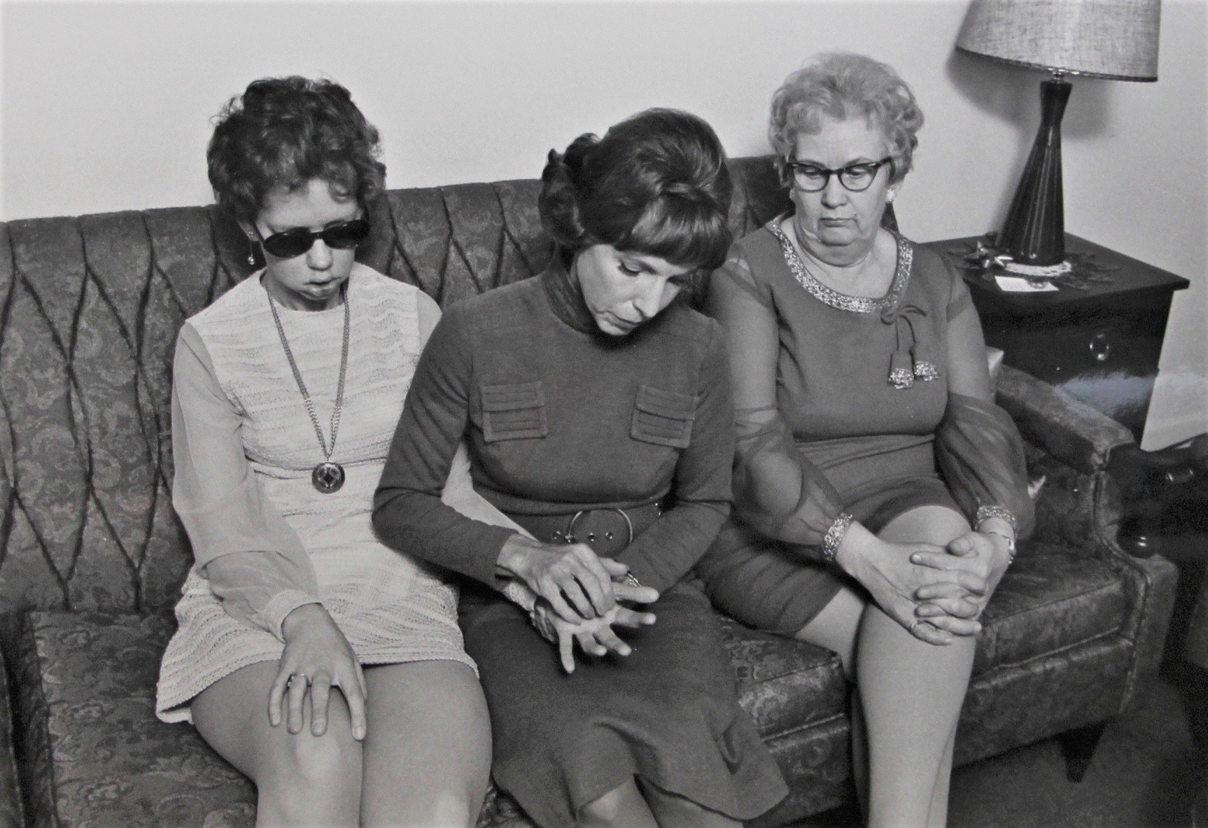 Mae Brown and Joan McTavish sit beside each other on a couch. Another woman sits beside them watching as the pair communicate.