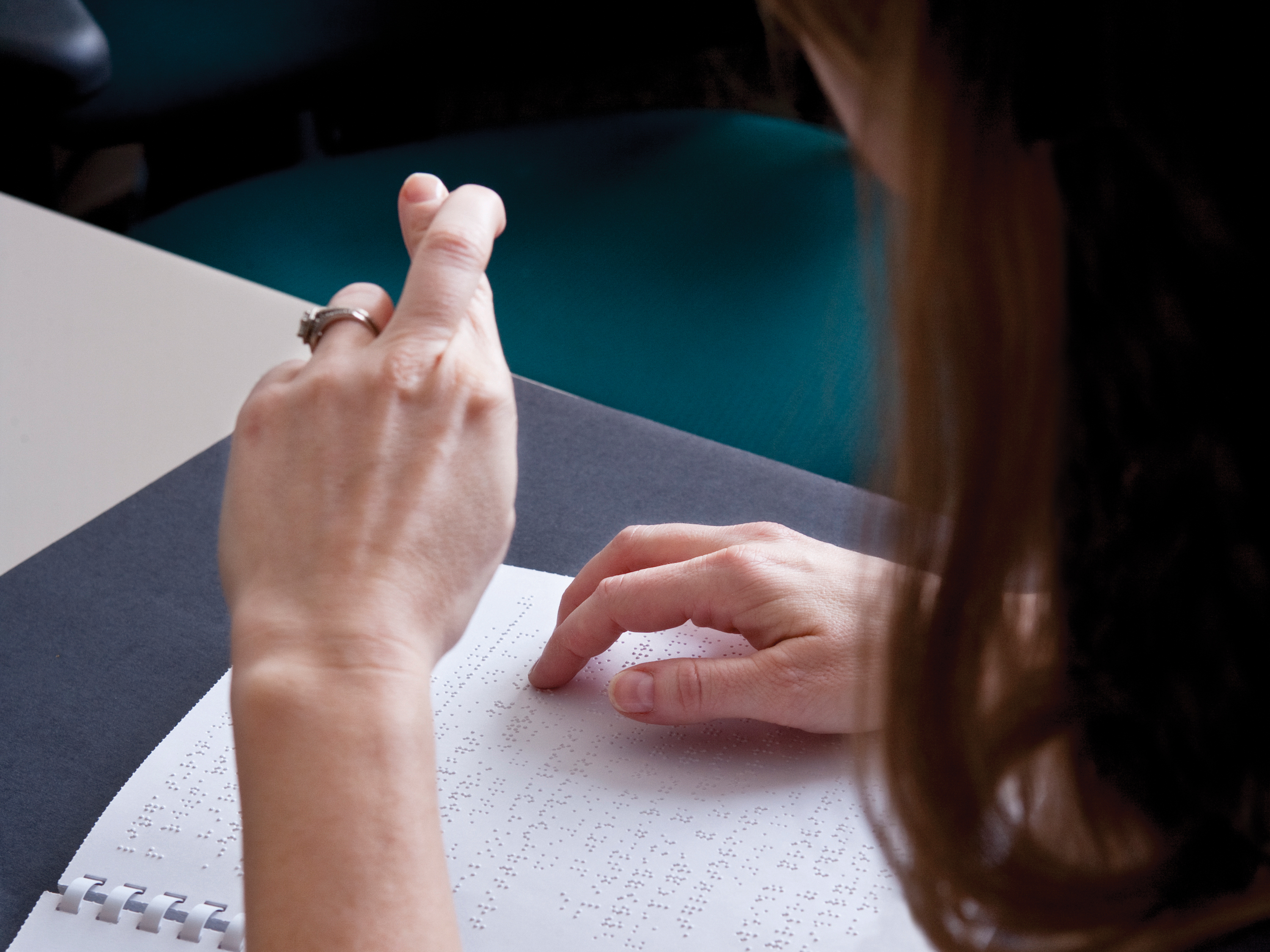 A person uses one hand to read braille, and the other to demonstrate sign language.