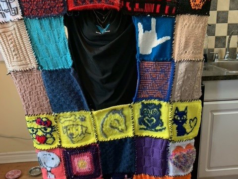 A multi-coloured quilt of yarn squares held up by a London DBCS staff member.