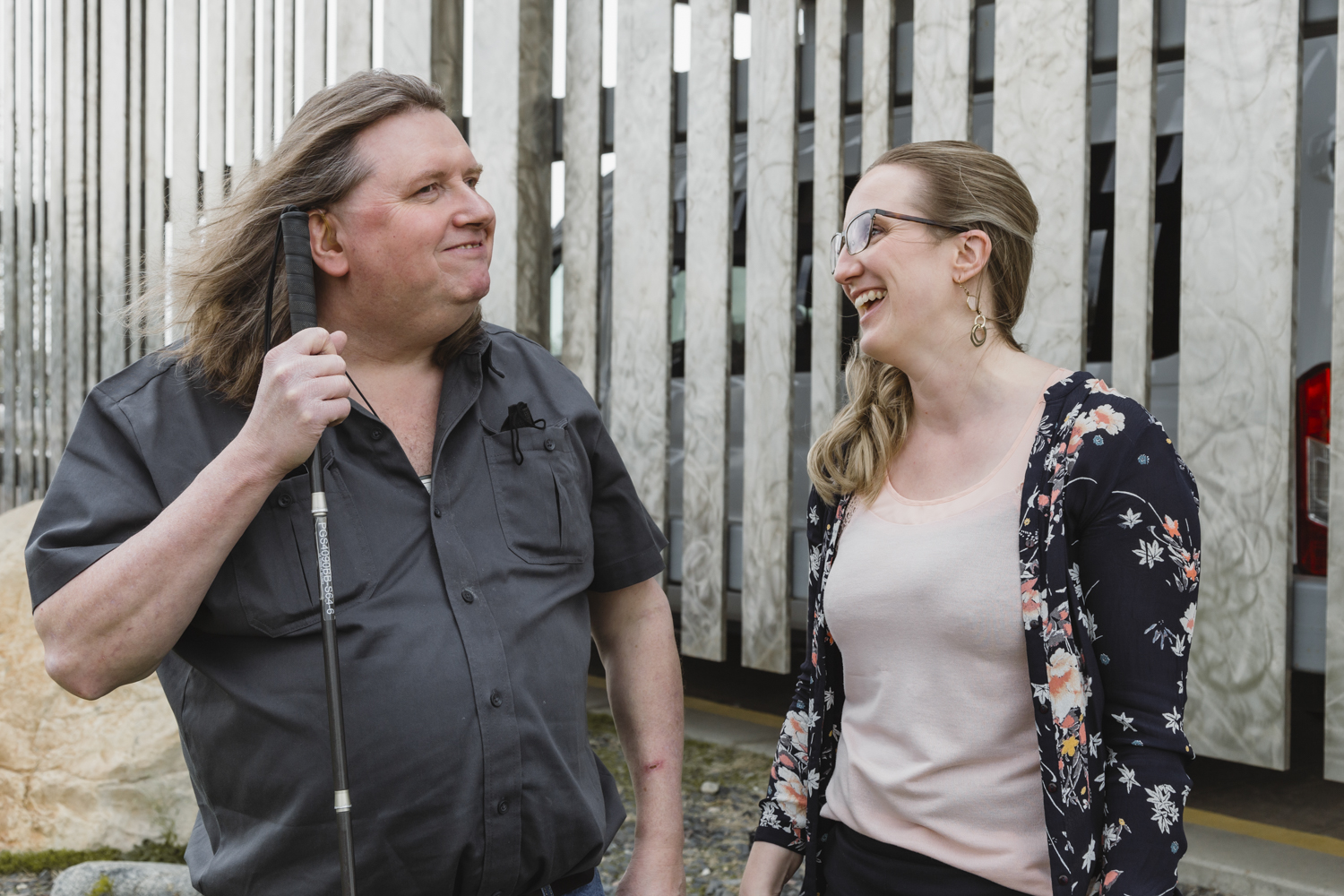 A DBCS client smiles while holding his cane. An intervenor stands beside him, with a big smile on her face.