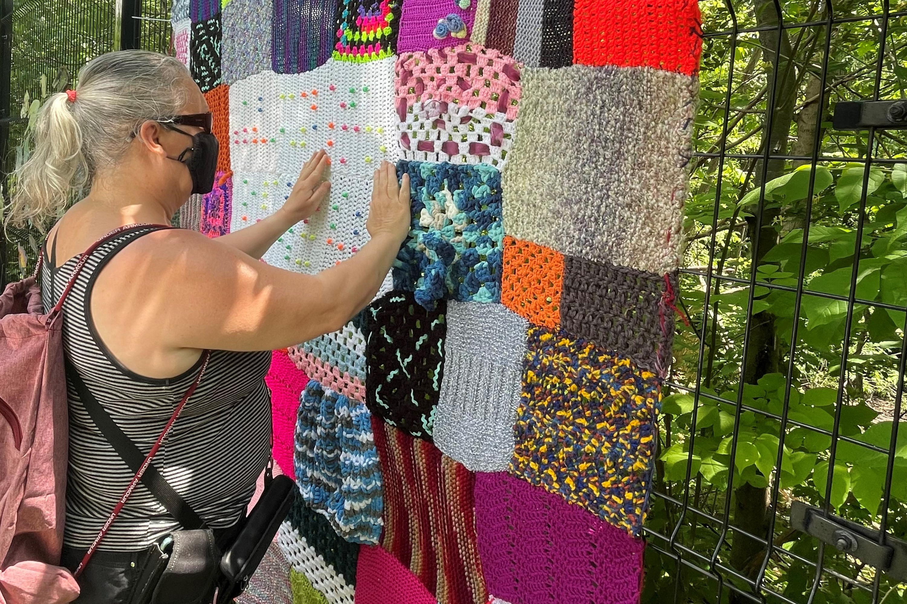 A woman feels the texture of a multi coloured yarn blanket
