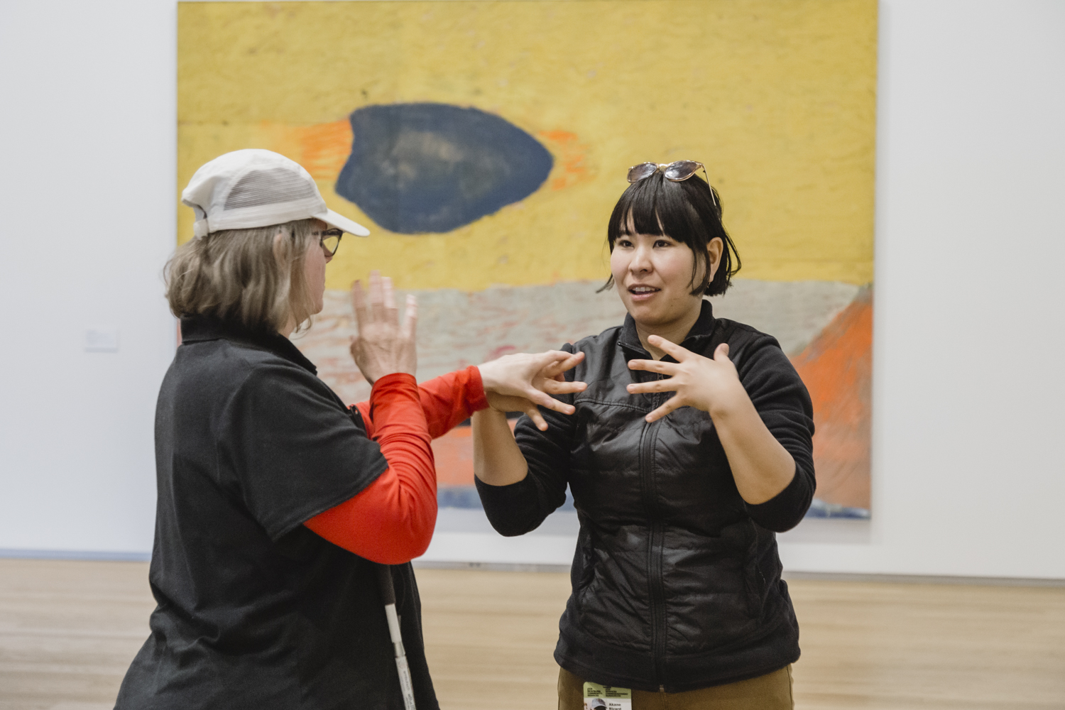 An intervenor uses tactile sign language to communicate with a Deafblind client at an art gallery