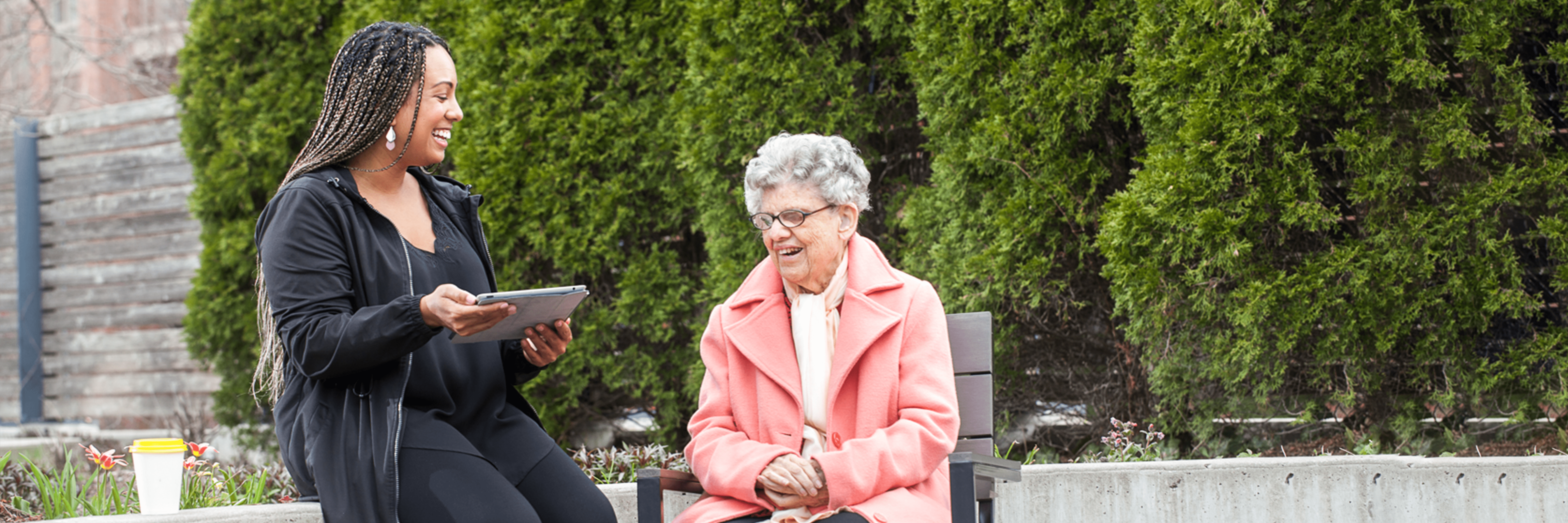 An intervenor sits beside a client outside. The intervenor uses a tablet to type large print notes to communicate with the client.