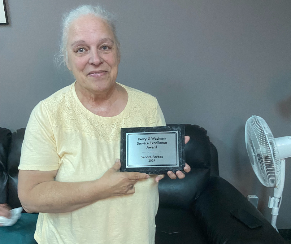 Sandra Forbes holds up an engraved plaque displaying her as the 2024 winner of the Kerry Wadman Award.