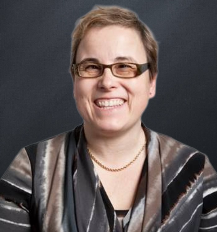 Headshot of Carrie. Carrie has short hair and is wearing glasses and a patterned blouse.