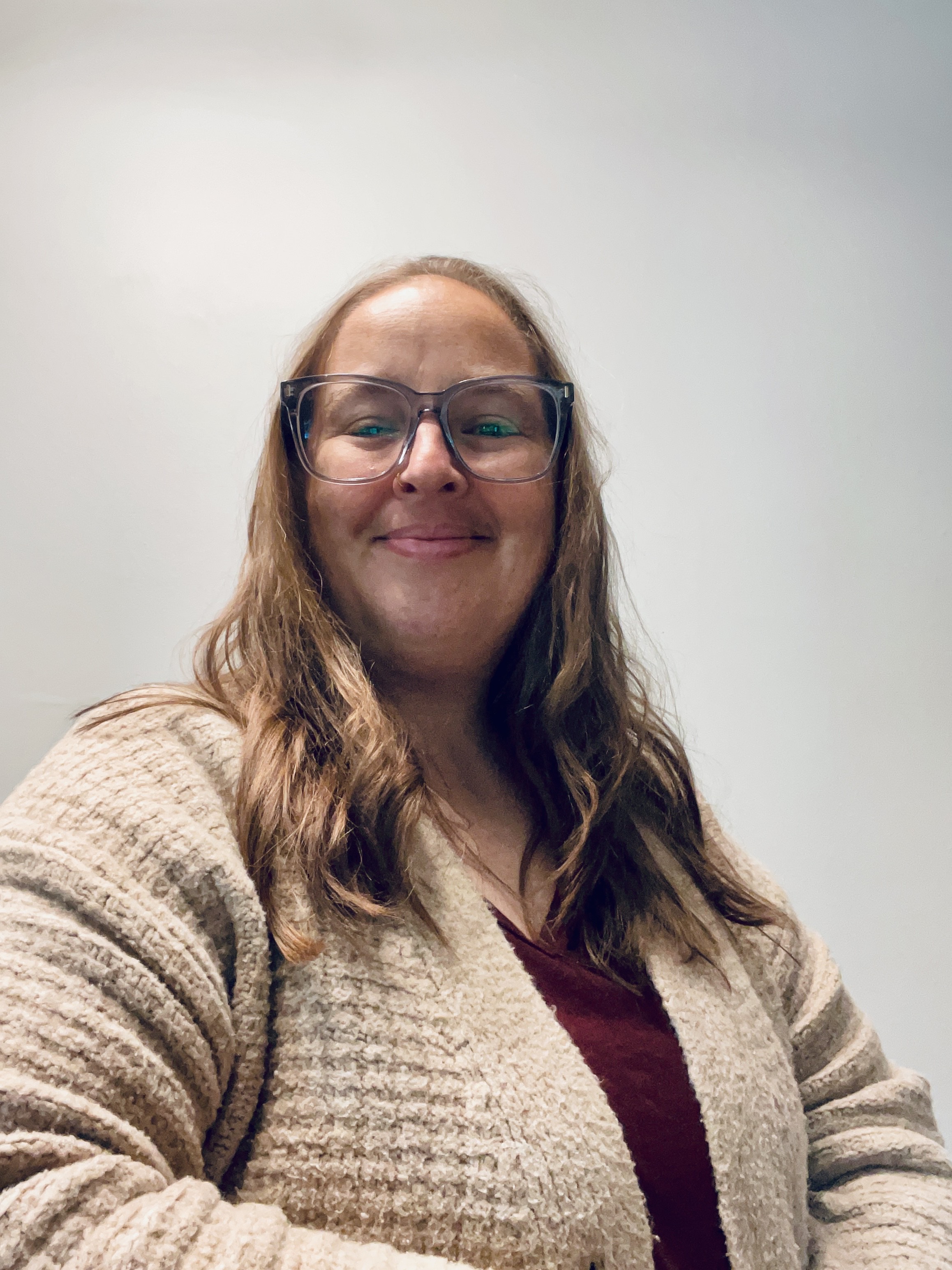 A smiling Jessica White poses for a photo. She wears a beige cardigan and burgundy t-shirt. She is smiling brightly.