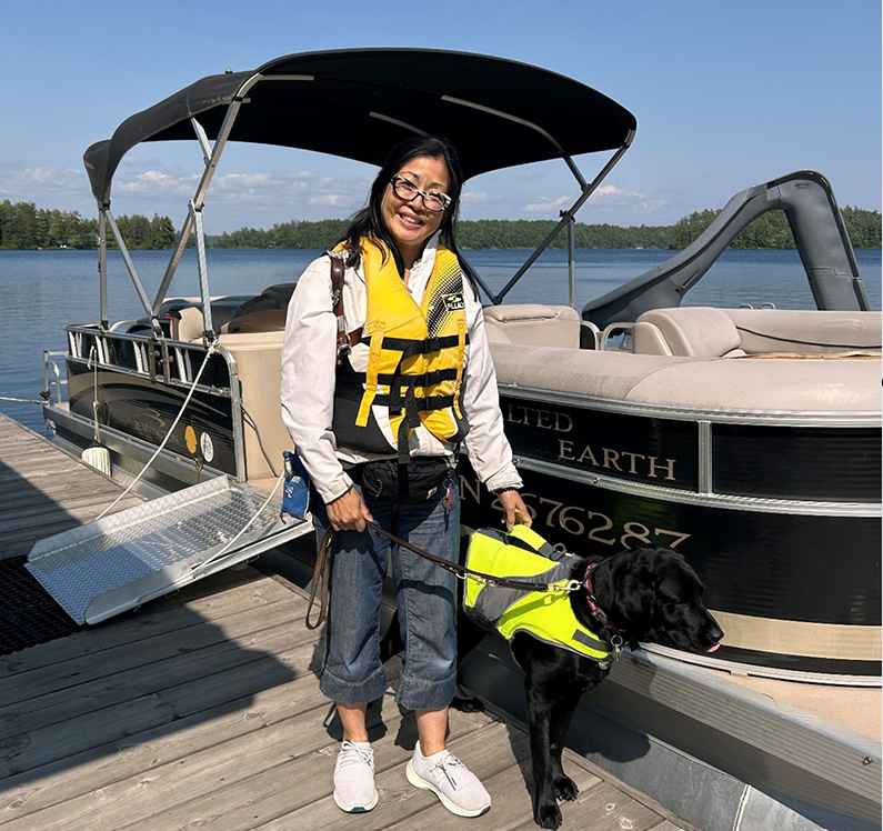 A smiling Dr. Kathryn Jung with her guide dog dismounting a boat on a summer day