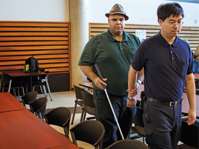 A man provides sighted guide to a person who is using a white cane.