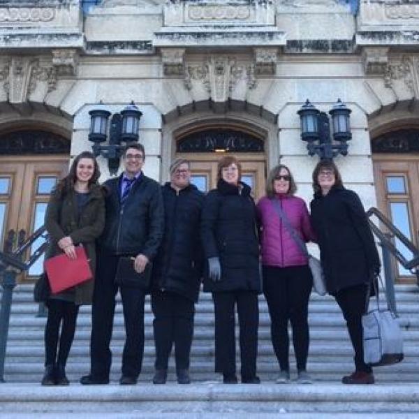 DBCS staff and government representatives from Saskatchewan stand outside a government building.